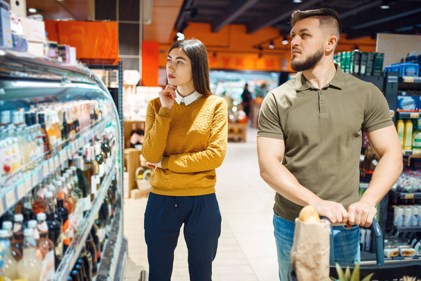 Family couple at the alcohol showcase in grocery store. Man and woman with cart buying beverages in market, customers shopping food and drinks - Photo, Image