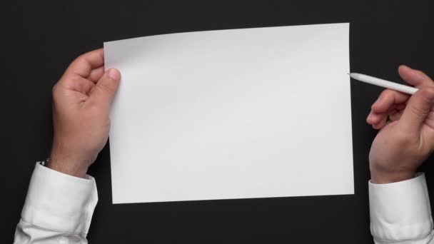 πάνω όψη ενός λευκού φύλλου χαρτιού και των χεριών ενός επιχειρηματία σε ένα μαύρο τραπέζι, λευκό πουκάμισο και ρολόι καρπού - Πλάνα, βίντεο