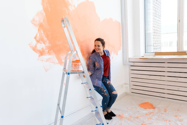 Mooi vrouwtje dat de muur schildert met verfroller. Portret van een mooie jonge vrouw die een muur schildert in haar nieuwe appartement. Opknappen en renoveren. - Foto, afbeelding