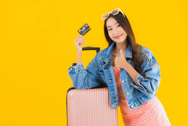 Portret pięknej młodej azjatyckiej kobiety z bagażem torba podróżna z paszportem i biletem na pokład na żółtym odizolowanym tle - Zdjęcie, obraz