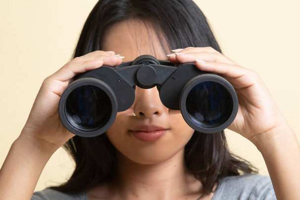 Young Asian woman with binoculars   on beige background - Foto, afbeelding