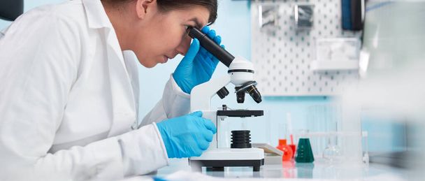 Vrouwelijke laboratoriumtechnicus kijkt naar microscoop in laboratorium. - Foto, afbeelding