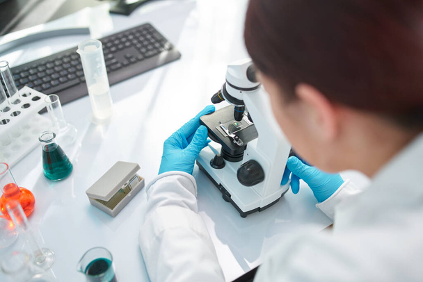 Γυναίκα βοηθός εργαστηρίου κοιτάζοντας μέσα από μικροσκόπιο στο εργαστήριο, closeup. - Φωτογραφία, εικόνα