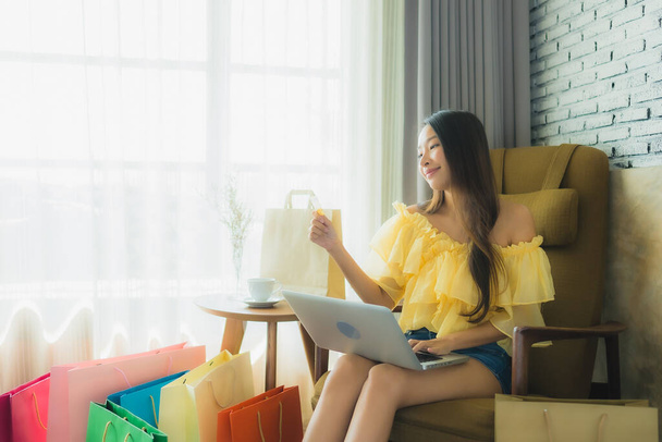 Portret jonge aziatische vrouw met behulp van laptop voor online winkelen met koffiebeker en boek in de woonkamer interieur - Foto, afbeelding