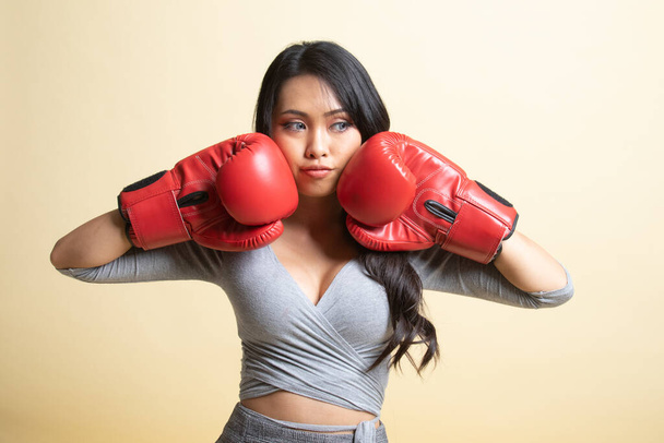 Young Asian woman with red boxing gloves   on beige background - Foto, afbeelding