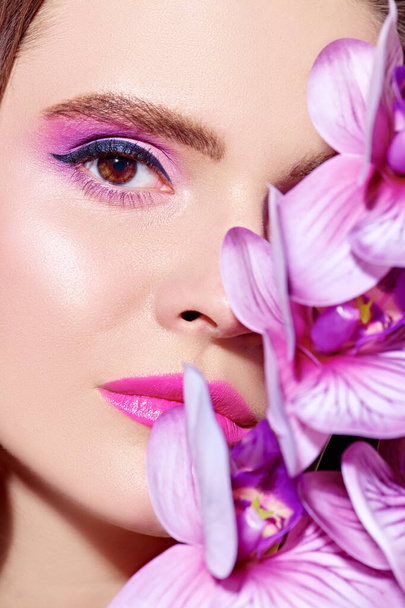 Close-up portrait of a beautiful romantic young woman with orchid flowers. Make-up and cosmetics. Beauty and health care. - Foto, Bild