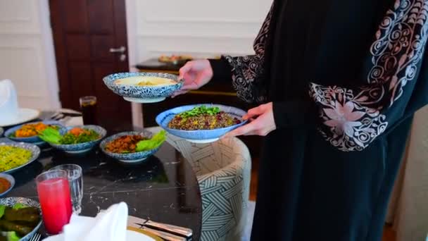 Das islamische Fest Eid ul-Fitr markiert das Ende des islamischen Fastenmonats Ramadan. Traditionelle östliche Speisen und Mahlzeiten stehen auf dem Tisch. Frau stellt Teller mit Essen auf den Tisch - Filmmaterial, Video