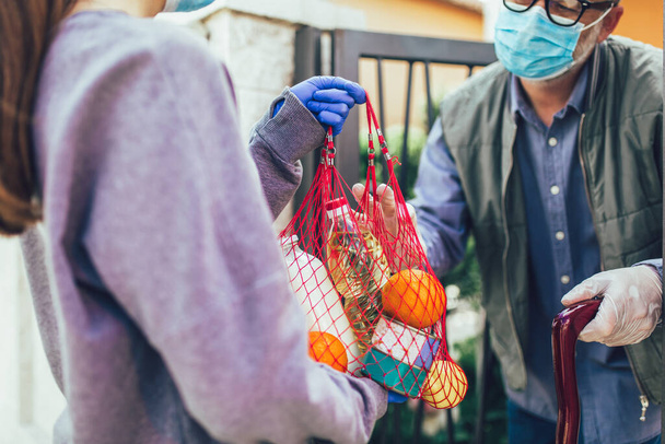 Adolescente ragazza sta consegnando alcuni generi alimentari ad una persona anziana, durante l'epidemia di coronovirus, COVID-19. - Foto, immagini