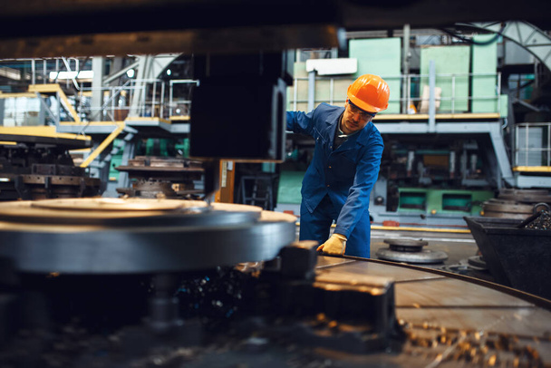 Тернер в форме и шлеме, стоящий на автоматизированном токарном заводе. Промышленное производство, металлообработка, энергетика
 - Фото, изображение