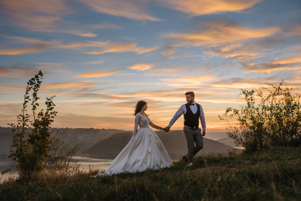 Der Bräutigam führt die Braut bei Sonnenuntergang an der Hand. - Foto, Bild