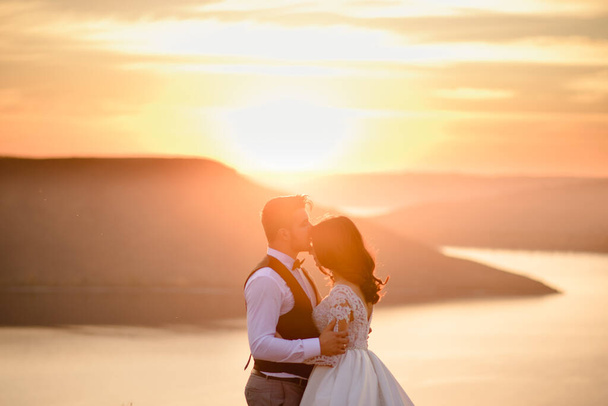 A noiva eo noivo estão abraçando no fundo do lago durante o pôr do sol
. - Foto, Imagem