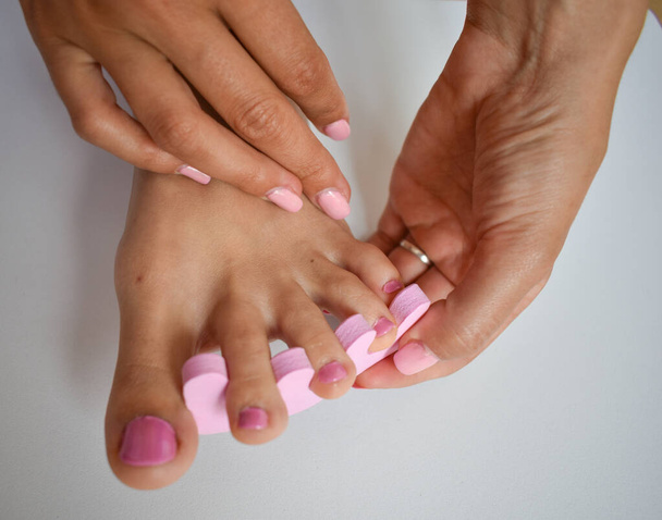 Female foot having a pedicure, putting pink nail polish on the nails of the feet and hands - Photo, Image