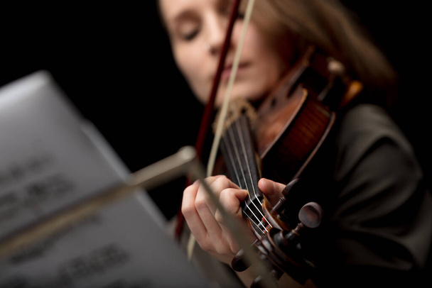 Γυναίκα παίζει ένα κλασικό βιολί κατά τη διάρκεια ενός ρεσιτάλ σε ένα κοντινό πλάνο περικοπεί χαμηλή γωνία με εστίαση στα δάχτυλά της στις χορδές - Φωτογραφία, εικόνα