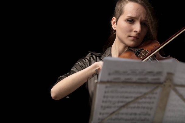 Жінка скрипаль грає в класичному записі на бароковій скрипці, переглянутій на вершині музичної партитури на латунній підставці під час живого виступу
 - Фото, зображення