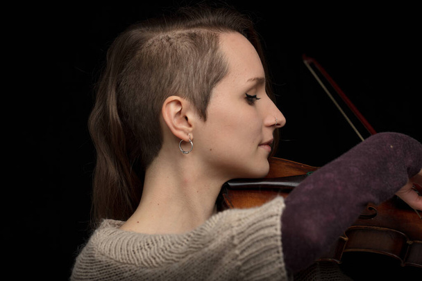 Věrný ženský houslista s moderním účesem hrající na barokní housle v detailním profilovém snímku hlavy nad černou - Fotografie, Obrázek