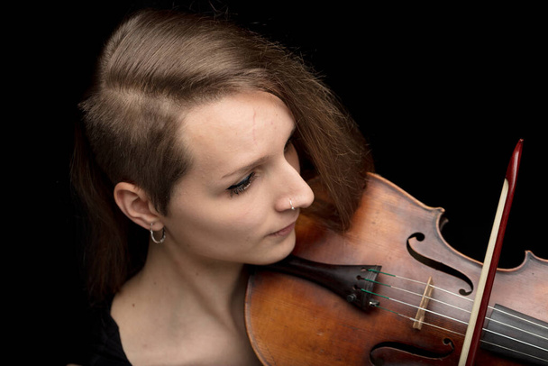 Jonge vrouw met modern kapsel spelen van een klassieke viool tijdens een optreden tegen een donkere achtergrond in een close-up hoge hoek uitzicht - Foto, afbeelding