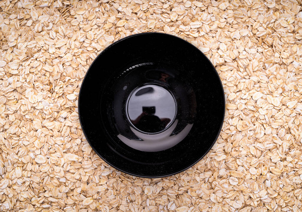 Natural oatmeal flakes, healthy food ingredients with vitamins. Background from a mumps, black plate in the center. - Photo, Image