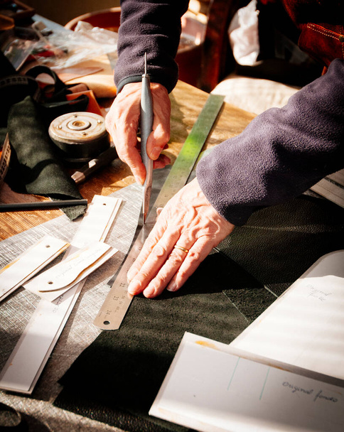 lederen vakman snijden van een stuk leer met een mes - Foto, afbeelding