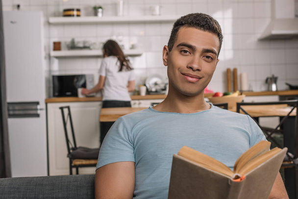 enfoque selectivo de hombre de raza mixta feliz celebración de libro en casa
 - Foto, Imagen