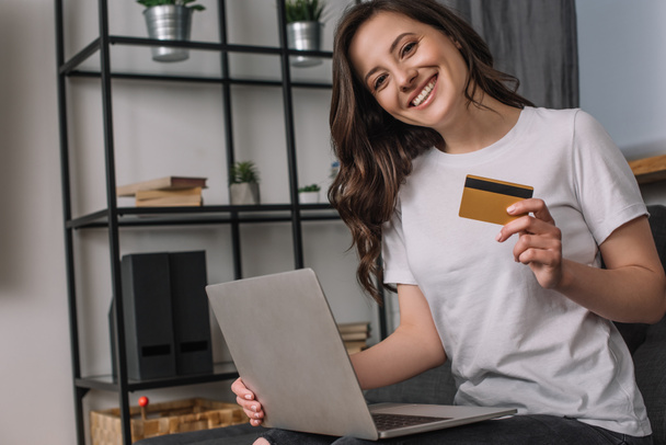 young and happy woman holding credit card near laptop - Фото, изображение