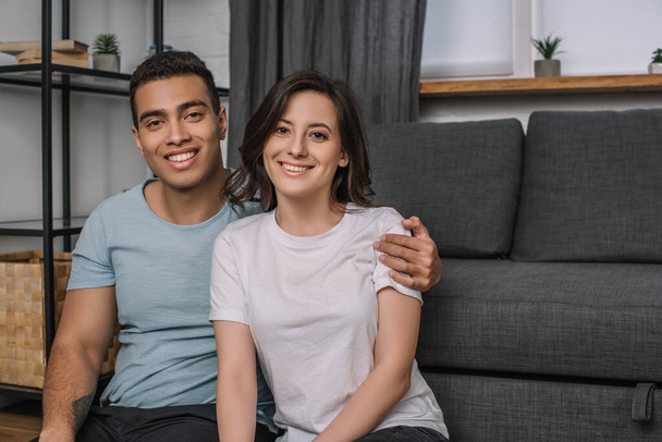 happy mixed race man hugging attractive and smiling girl at home - Foto, Imagem