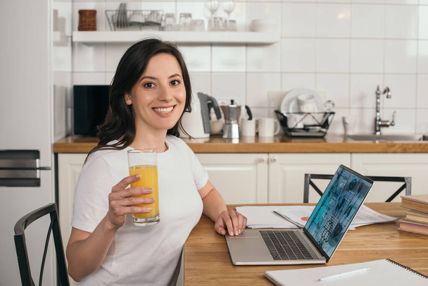 mulher feliz segurando vidro de suco de laranja perto de laptop com site médico
 - Foto, Imagem