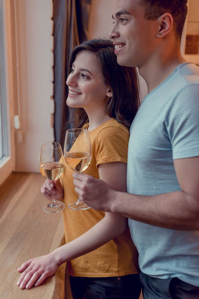 cheerful interracial couple holding glasses with white wine at home - Zdjęcie, obraz