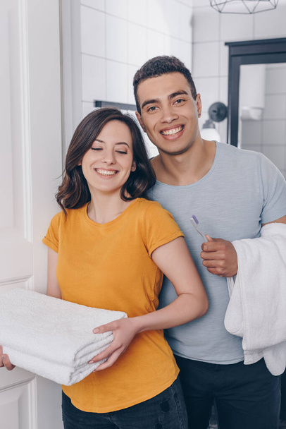 happy multiracial couple holding towels in bathroom  - Foto, afbeelding