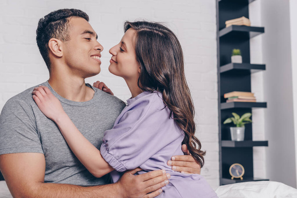 mixed race man and cheerful woman hugging at home - Fotografie, Obrázek