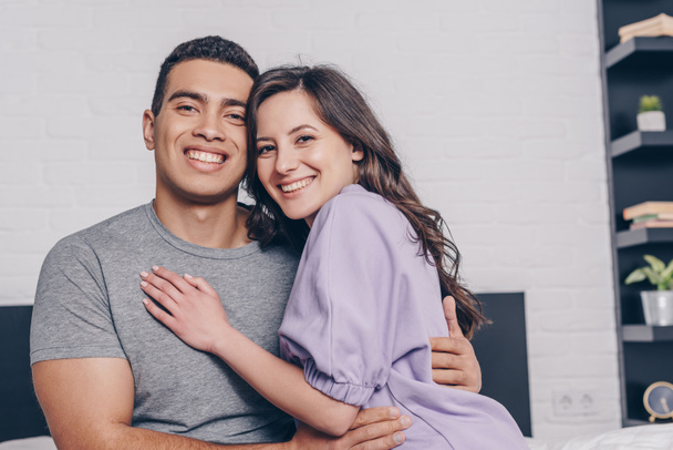 positive mixed race man and cheerful woman hugging at home - Photo, Image