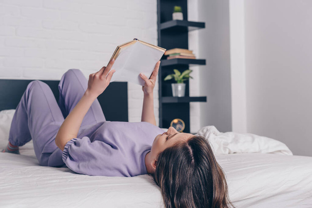junge Frau liegt auf Bett und liest Buch  - Foto, Bild