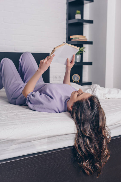 attractive young woman lying on bed and reading book  - Valokuva, kuva