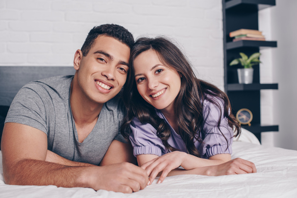 cheerful and young multiracial couple smiling in bedroom  - Foto, afbeelding