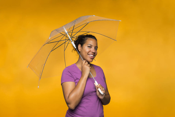 young attractive mixed race woman holding an umbrella wearing a purple shirt against a yellow background - Photo, image