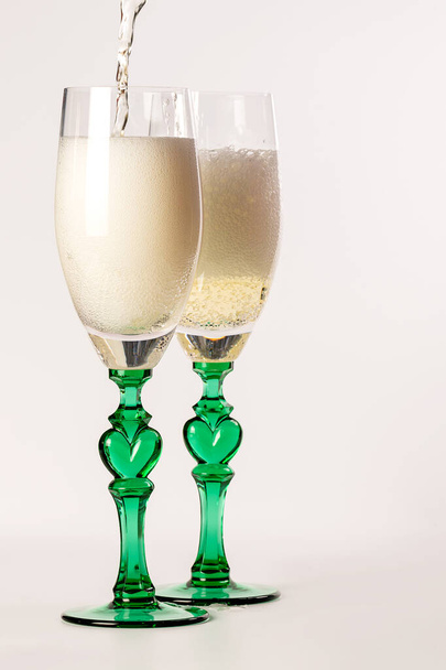 Two glasses of champagne and a bottle on a white background. Creative image with champagne bubbles sparkling in the sun. - Fotografie, Obrázek
