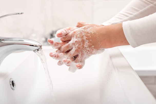 Mies tai nainen pesee kädet saippualla seistessään pesualtaalla kylpyhuoneessa
. - Valokuva, kuva