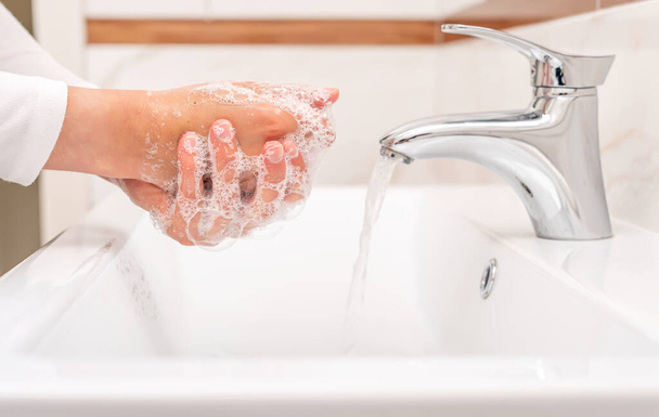 バスルームのシンクに立っている間に男か女は石鹸で手を洗う. - 写真・画像