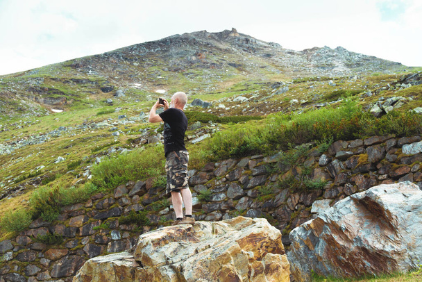 Een toerist fotografeert een prachtig uitzicht vanaf een hoogte op zijn smartphone. Een bebaarde man maakt een foto van het landschap. - Foto, afbeelding