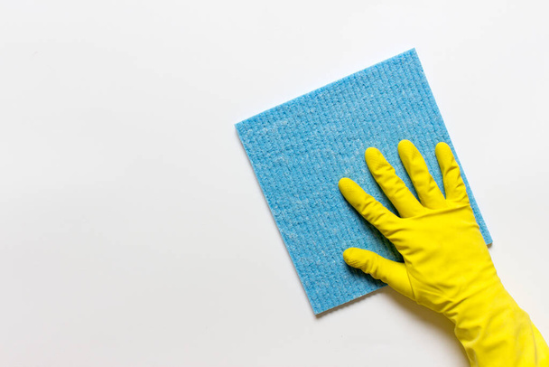 Female hand in yellow rubber glove with blue microfiber cloth on white background. Photo with copy blank space. - Fotografie, Obrázek
