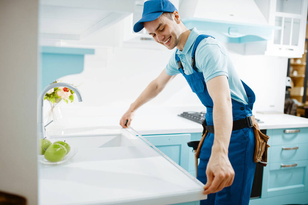 Muž nábytkář v uniformě měří stolní desku v kuchyni. Handyman instalace garniture, opravy doma - Fotografie, Obrázek