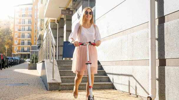 Beautiful young woman in skirt riding on scooter at early morning - Photo, Image