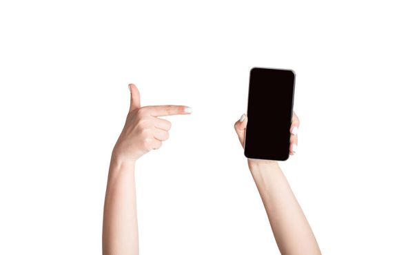 Dziewczyna wskazująca na telefon komórkowy z pustym ekranem, odizolowana na biało. Mockup dla Twojej strony internetowej lub projektu aplikacji - Zdjęcie, obraz