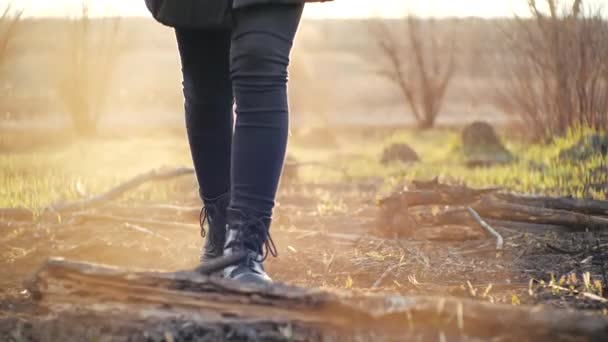 Fotografía cinematográfica frente a una joven paseando con leggings de moda y elegantes botas negras de suela alta en el suelo de ceniza después del fuego contra un campo bajo el atardecer. La persona pisa la hierba quemada en primavera
. - Imágenes, Vídeo