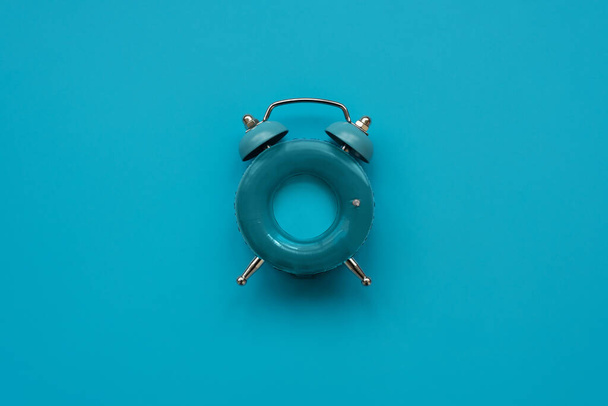 Vacation time. Blue alarm clock as swimming ring form on blue background. Top view. Copy space - Фото, изображение