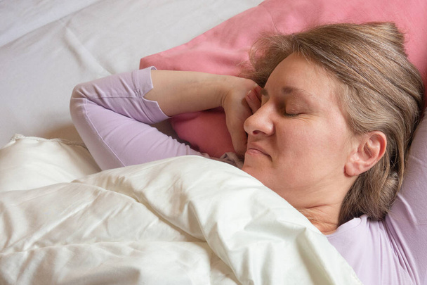 女は後ろで寝ている。40歳の女性のクローズアップポートレートで落ち着いたとリラックスした顔の睡眠ピンクの枕 - 写真・画像