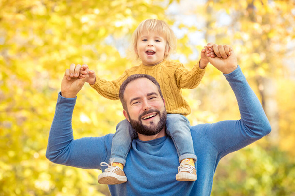 Happy family having fun outdoor in autumn park. Father and son against yellow blurred leaves background - Photo, image