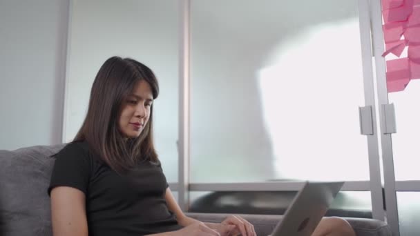 Азиатская молодая женщина-фрилансер работает из дома, любит улыбаться сидя на диване, социальная дистанция, самообучение, учебная программа онлайн-курсов, продуктивный распорядок дня, онлайн-серфинг  - Кадры, видео