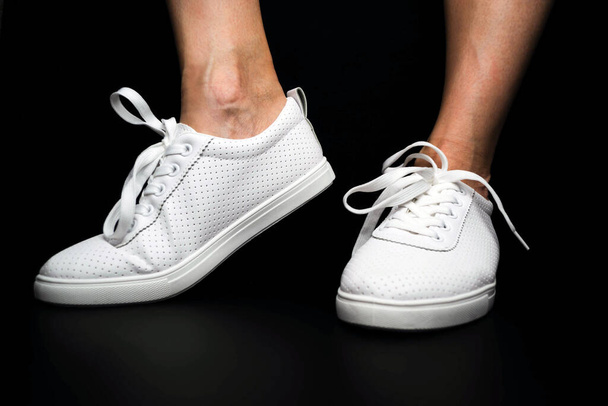Белые кроссовки одеты на ноги на черном фоне. Спортивная обувь
 - Фото, изображение