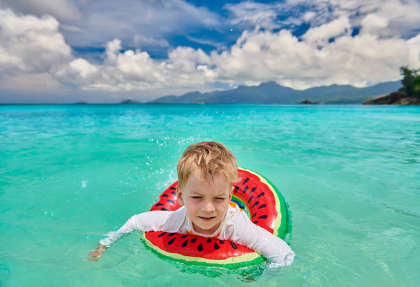 Three year old toddler boy on beach at Seychelles swimming with inflatable ring - Fotó, kép