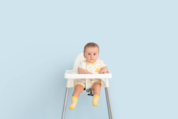 Cute little baby sitting on feeding chair against color background - Fotó, kép